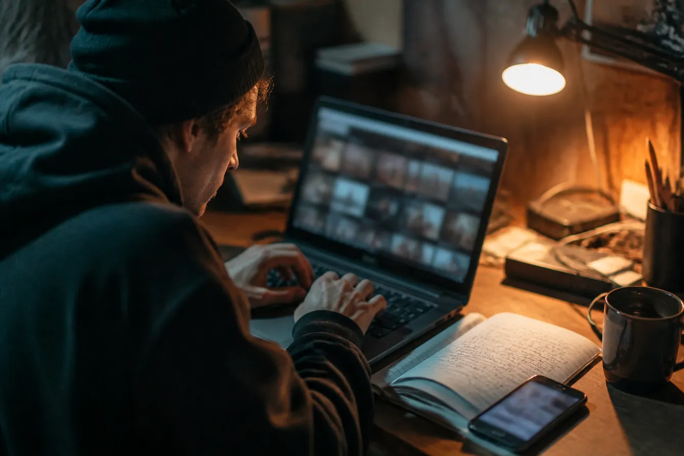 A person searches for dark web videos on a laptop in a cozy, warm-lit room, emphasizing safe browsing techniques.